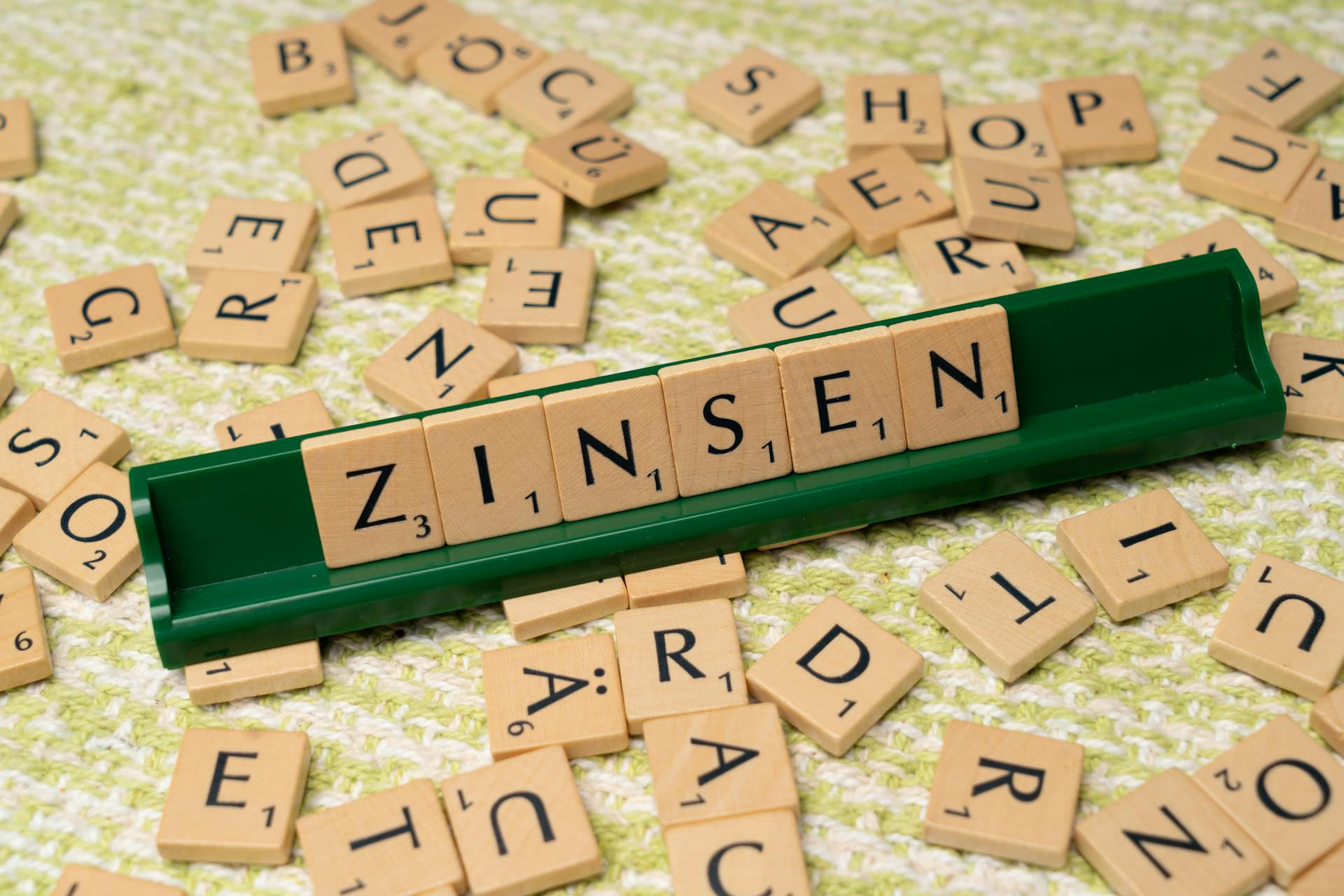 Wooden Scrabble pieces on a green tray spelling the German word 'Zinsen' meaning interest.