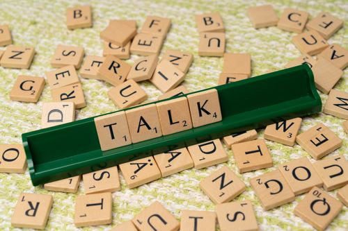Free Scrabble tiles arranged to spell 'Talk' on a green tray, surrounded by scattered tiles on a textured surface. Stock Photo
