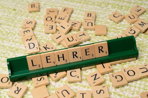 Free Wooden letter tiles spelling 'Lehrer' on a green rack, surrounded by scattered tiles. Stock Photo
