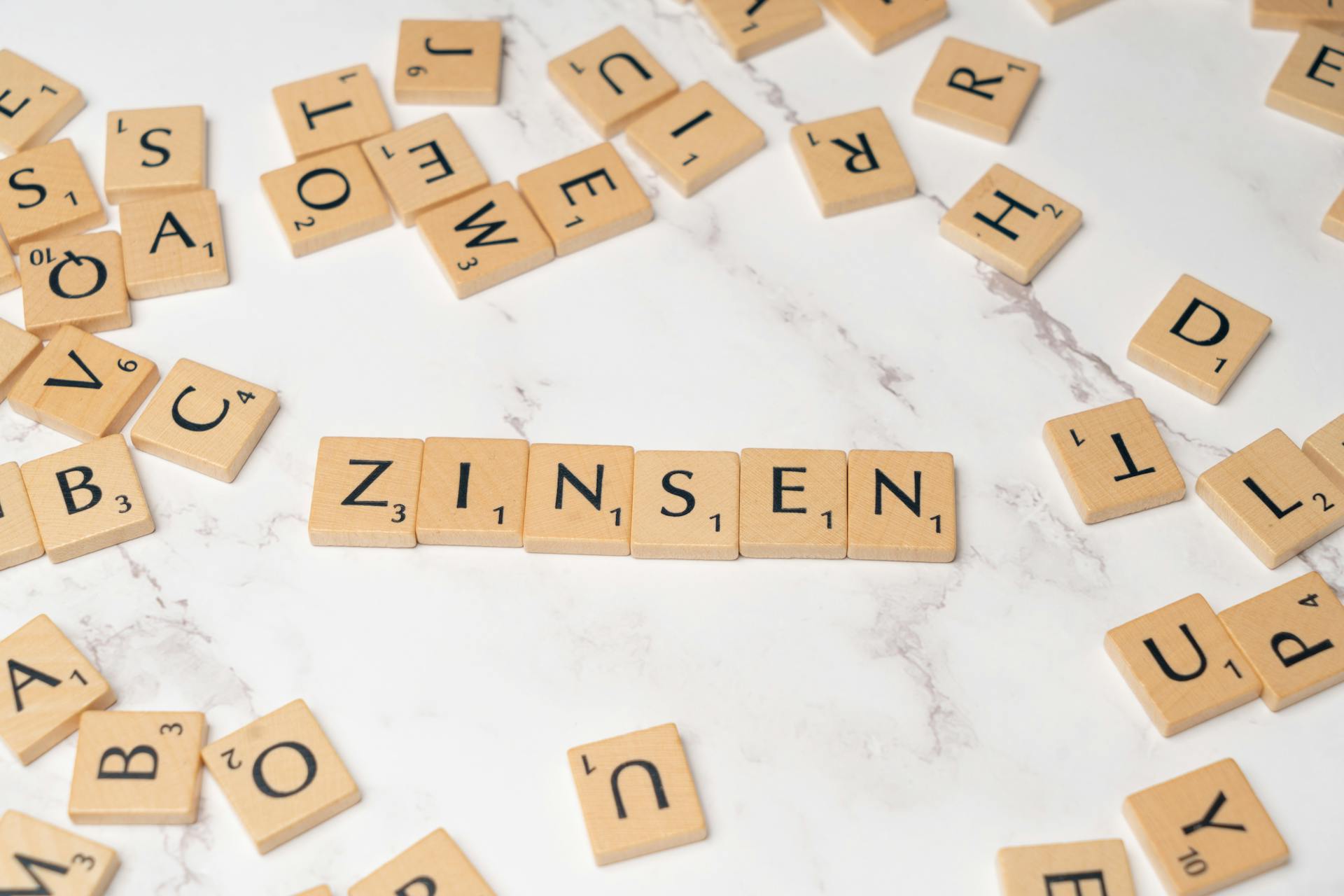 Scrabble tiles spelling 'Zinsen' on a marble surface with scattered tiles around, symbolizing interest rates.