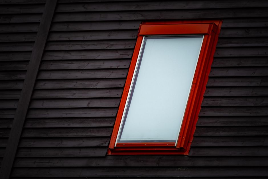 Close-up of a skylight with a red frame embedded in a dark wooden rooftop.