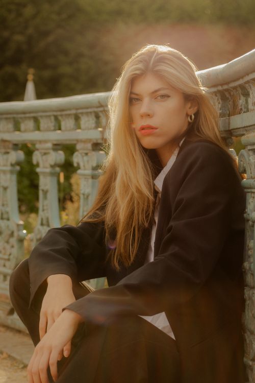Free Stylish woman in a black suit sitting outdoors with a serene expression, soft natural lighting accentuating her features. Stock Photo