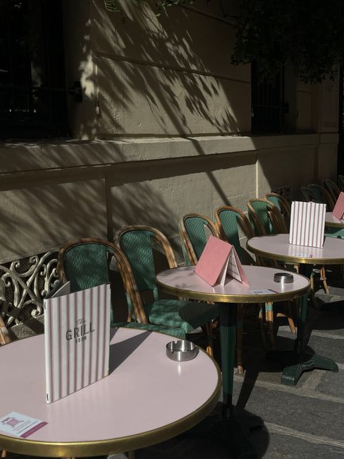 Sunlit café tables and chairs with menus and ashtrays on a sidewalk setting.
