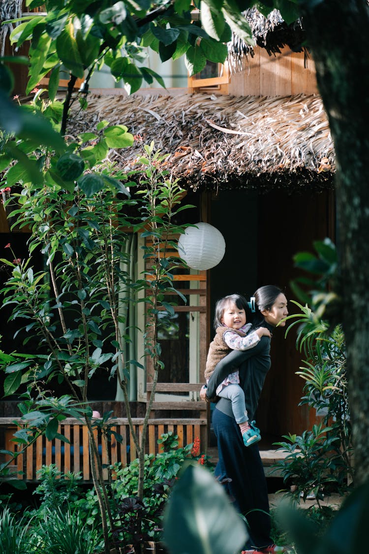 Mother Carrying Daughter By House