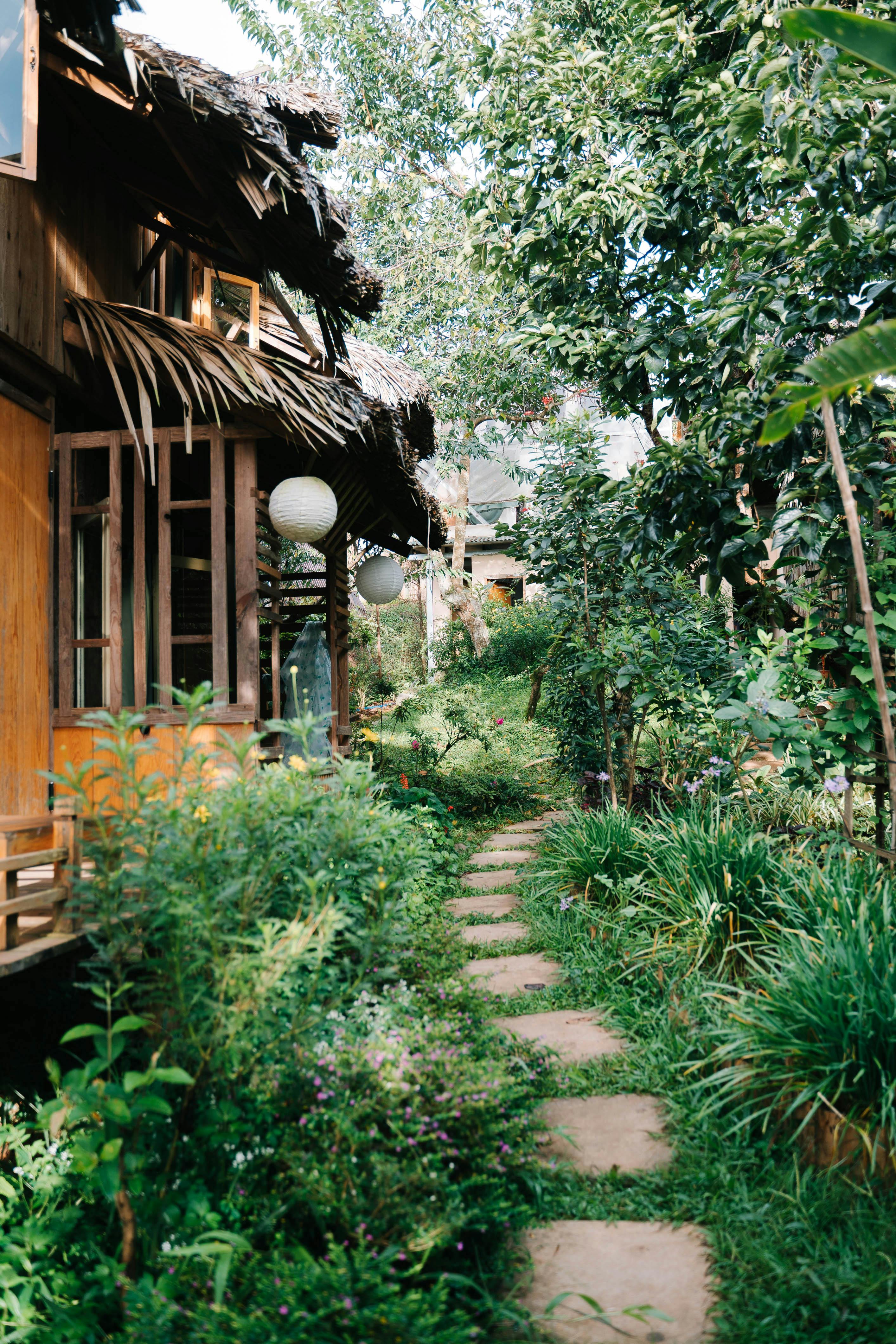 Peaceful garden path lined with lush greenery and rustic wooden houses.