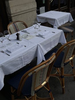 Chic outdoor restaurant setup with tablecloths, glasses, and rattan chairs.