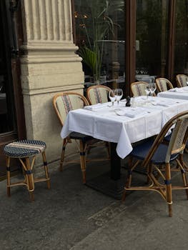 Charming outdoor cafe setup with chic chairs and table in a bustling urban environment.