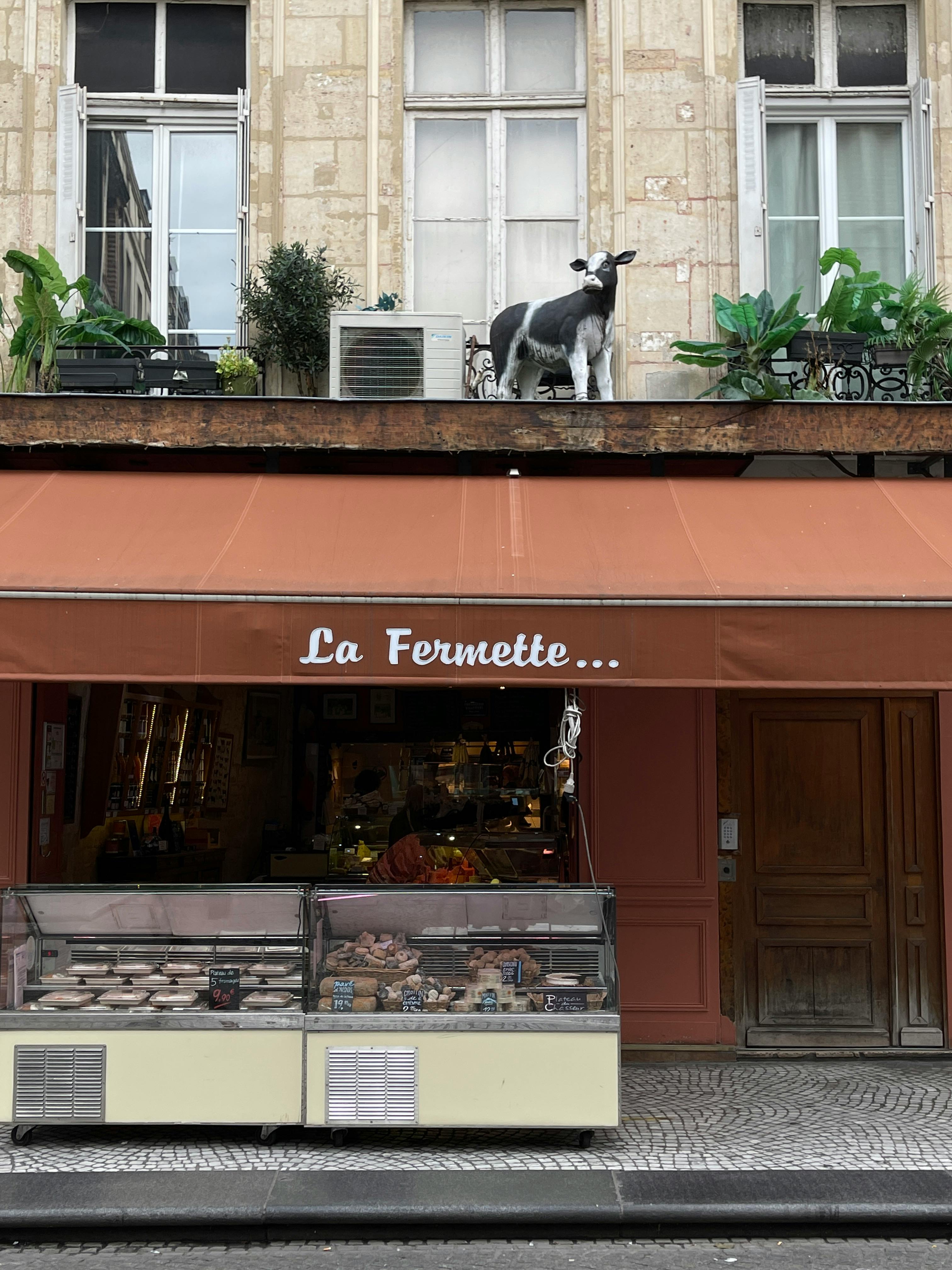 French shop exterior with cow sculpture and vibrant awning, offering an inviting urban atmosphere.