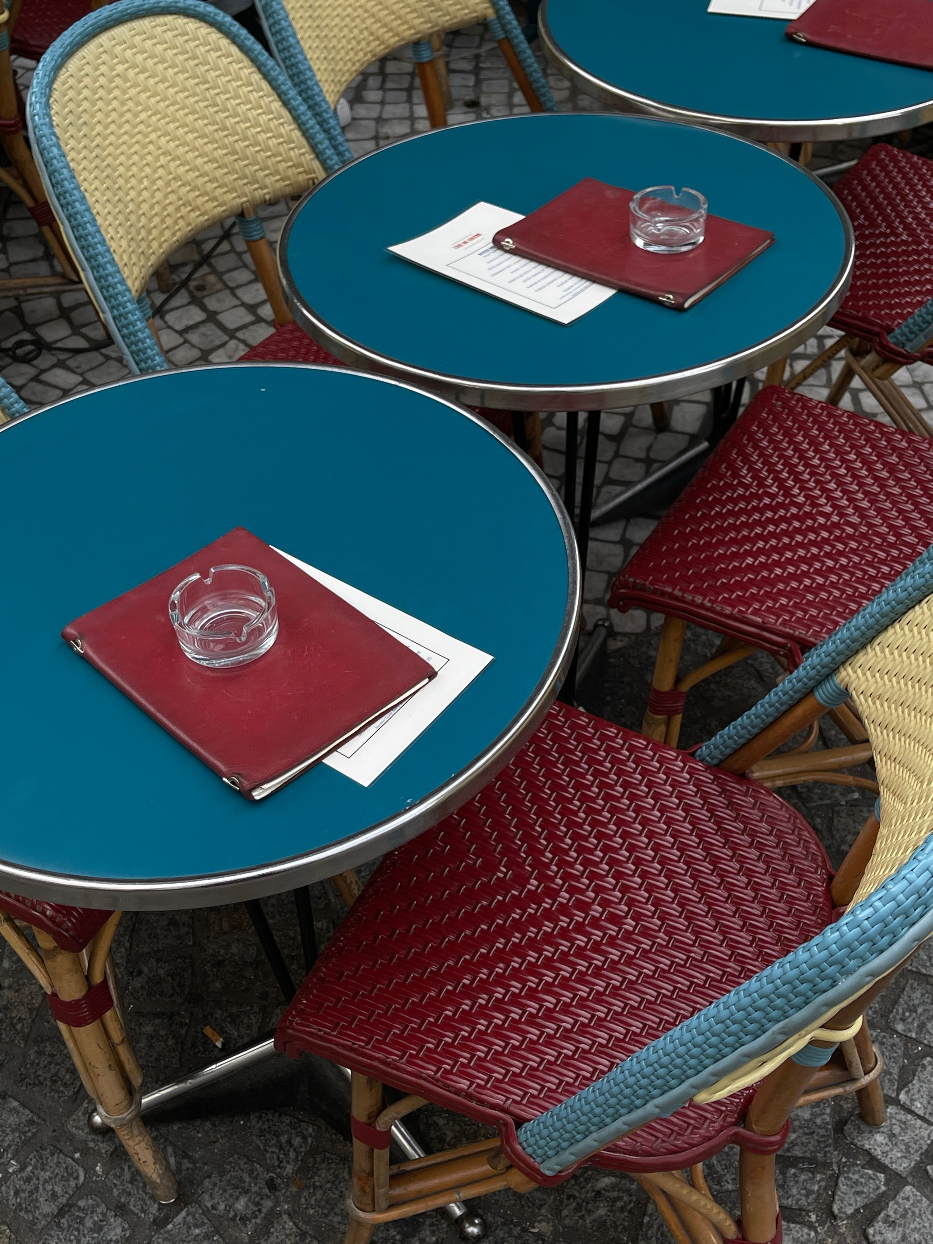 Colorful outdoor cafe tables with ashtrays and menus in an urban setting.