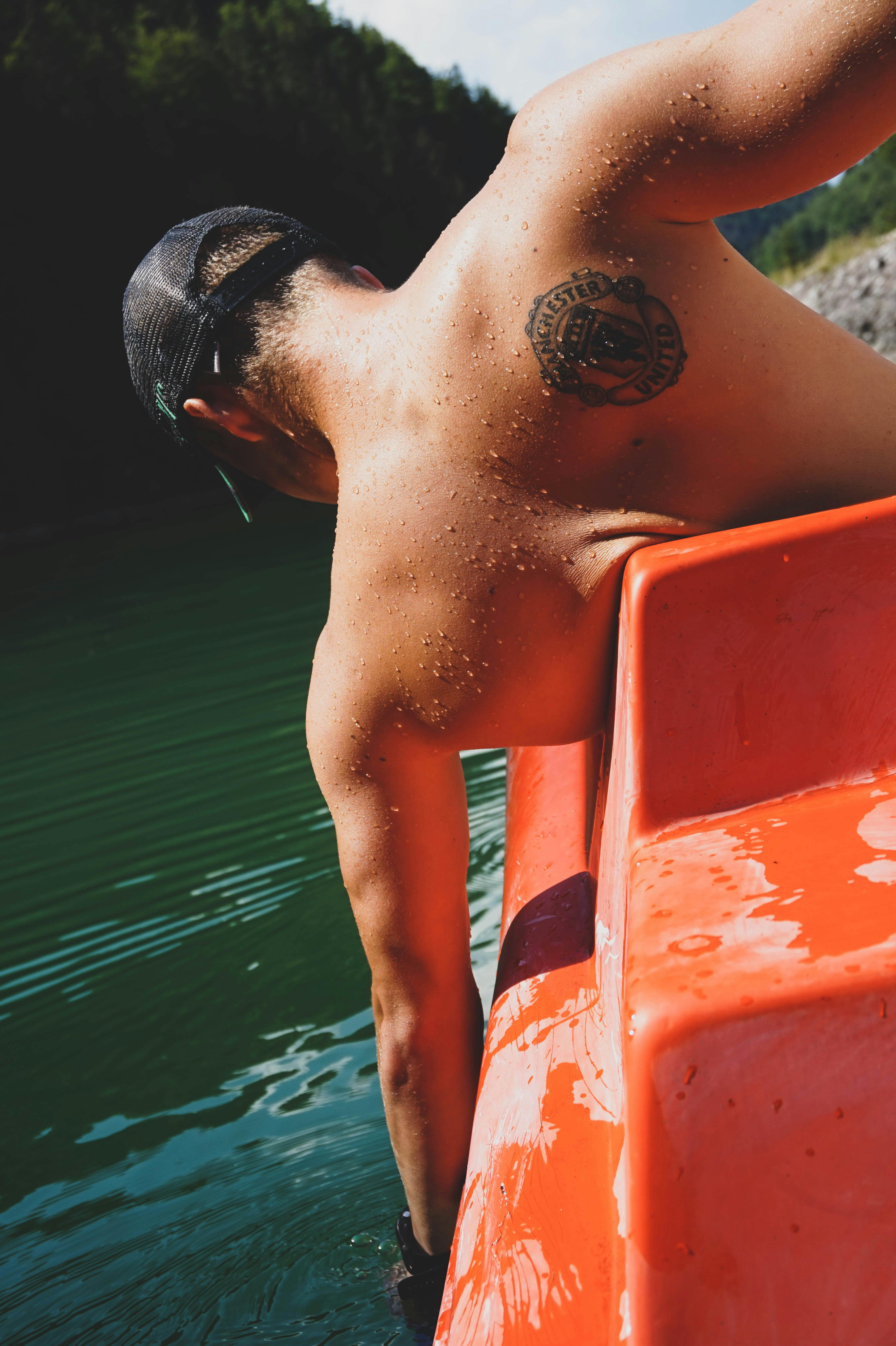 topless man sitting on boat near river