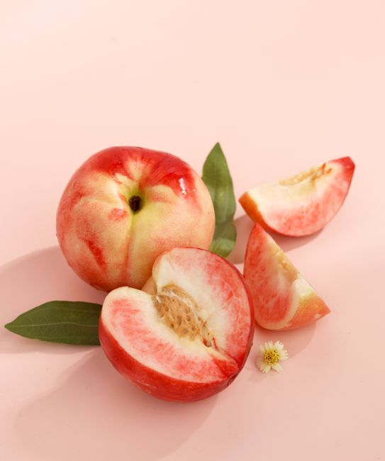 Delicious ripe white peaches, halved and whole, on a pink surface with green leaves.