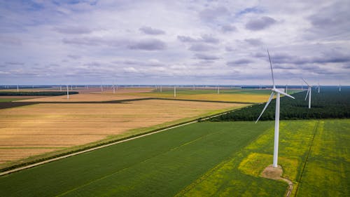 Wind turbines on a flat landscape with maintenance workers in high-visibility vests walking near the base of a turbine