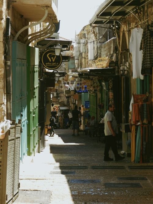Free A narrow, sunlit alley in an old city market, showcasing traditional architecture and vibrant street life. Stock Photo