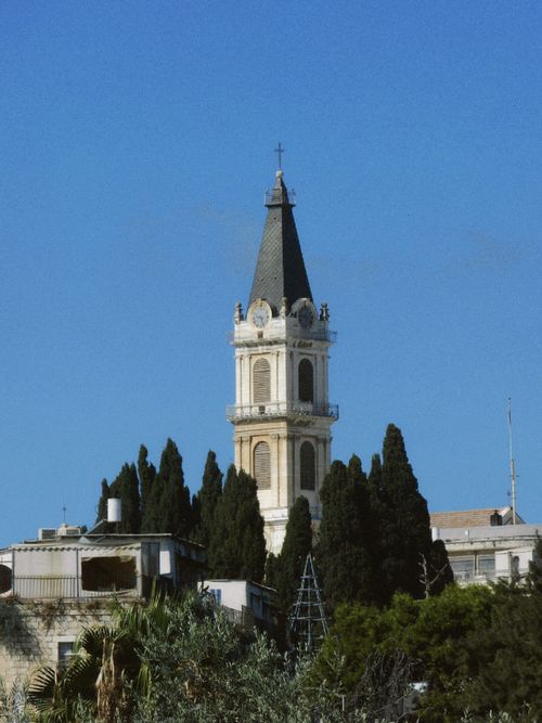 Free A historic church tower surrounded by greenery under a clear blue sky, showcasing traditional architecture. Stock Photo