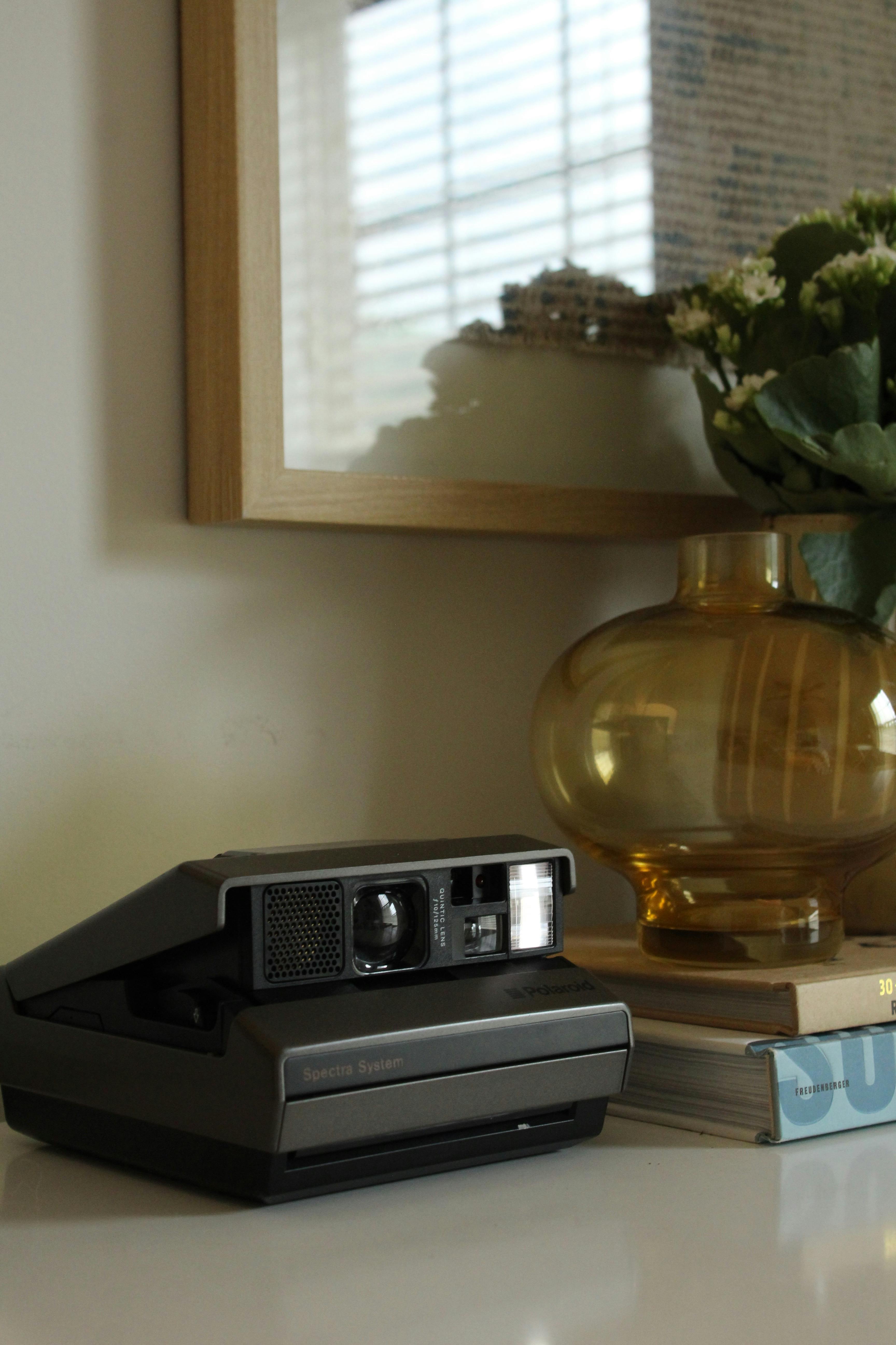 A vintage camera sits beside a glass vase with flowers, creating a nostalgic indoor setting.