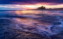 沿海城堡与海岸线上，日出色彩鲜艳，海浪宁静，景象十分壮观