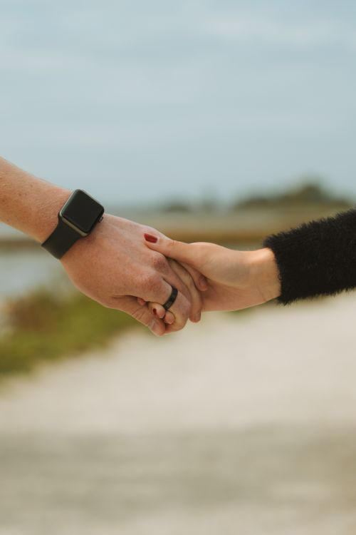 Free Close-up of a couple holding hands outdoors, showcasing a smartwatch. Intimate connection and technology theme. Stock Photo