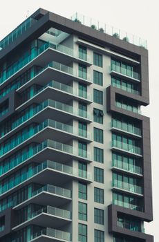 A sleek modern high-rise with turquoise glass facade and balconies.