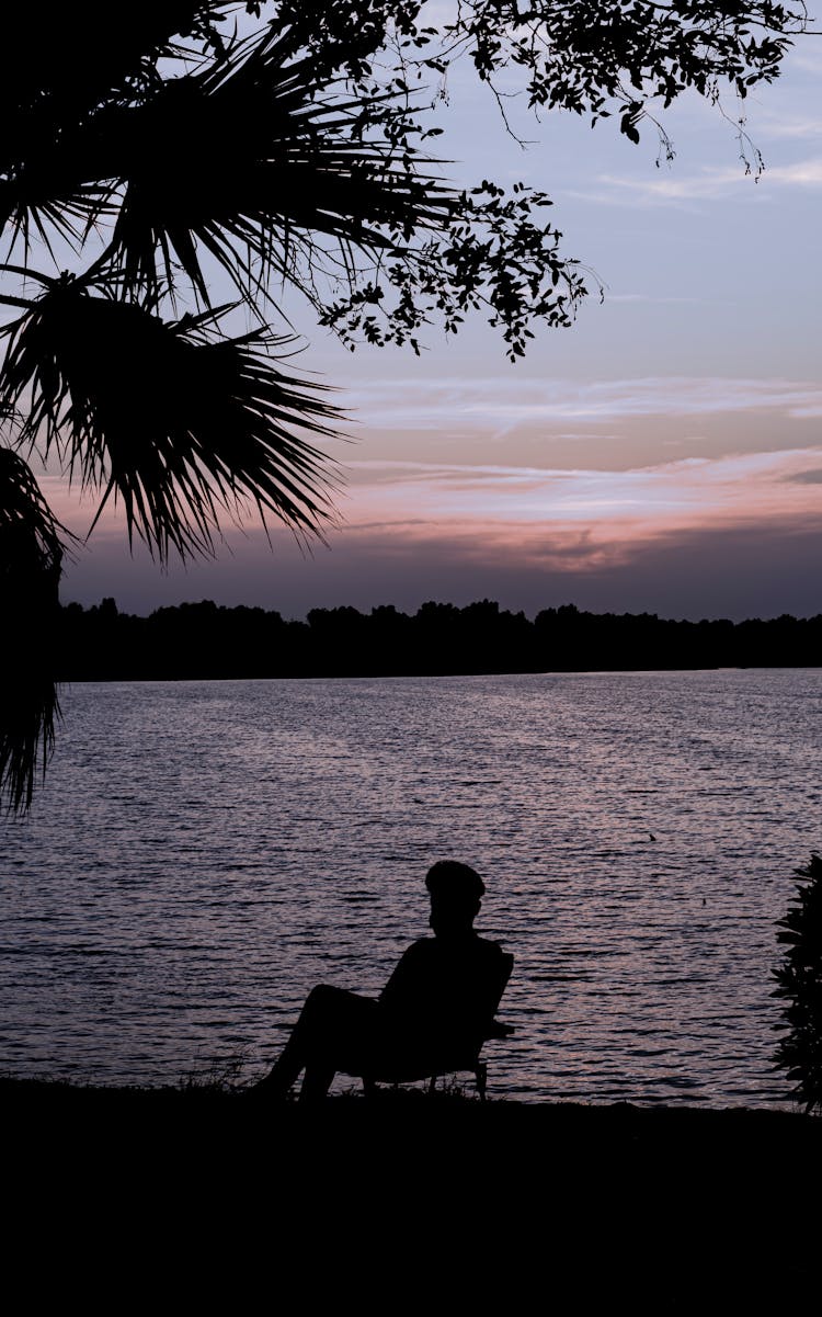 Silhouette Of A Person Sitting In A Chair At A Beach At Dusk