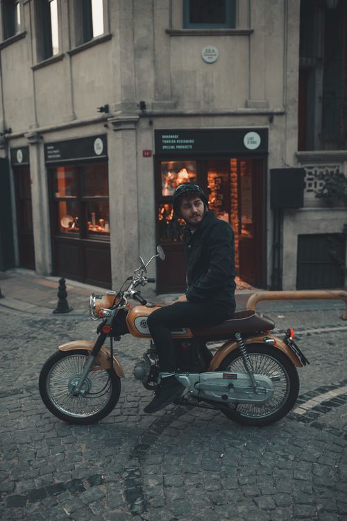 Free Young man in a black jacket sitting on a motorcycle on a cobblestone street at dusk. Stock Photo