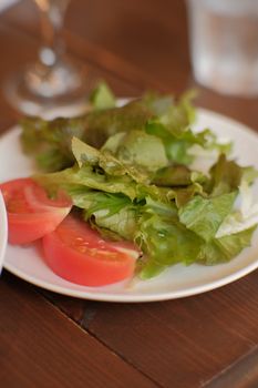 A fresh green salad with crisp lettuce and ripe tomato slices on a white plate.