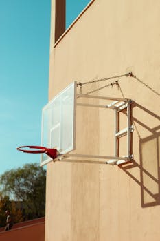 Street basketball hoop mounted on wall against clear sky.