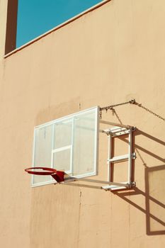 A minimalist shot of a basketball hoop mounted on a wall under clear skies, showcasing urban simplicity.