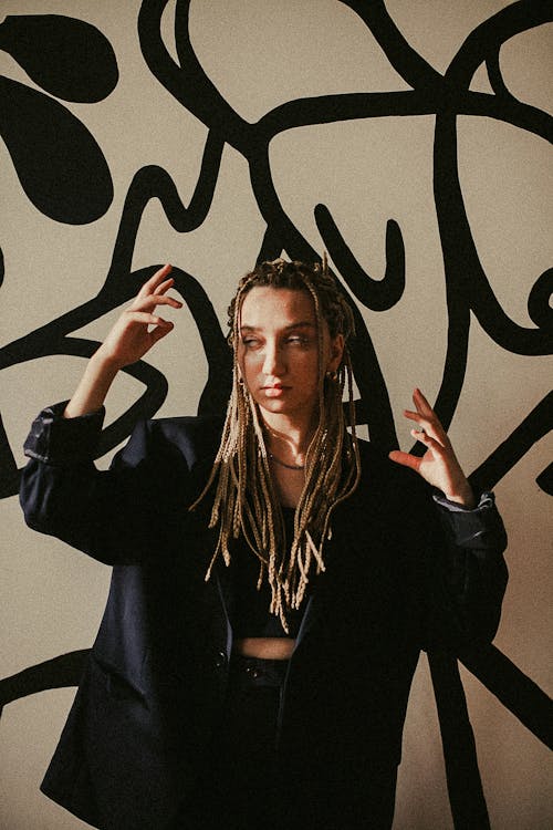 Young Woman with Dreadlocks Wearing a Black Blazer and Crop Top in Font of a Wall with a Drawing