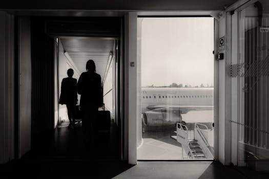 Silhouetted travelers walking through an airport jet bridge toward an airplane, conveying a travel mood.