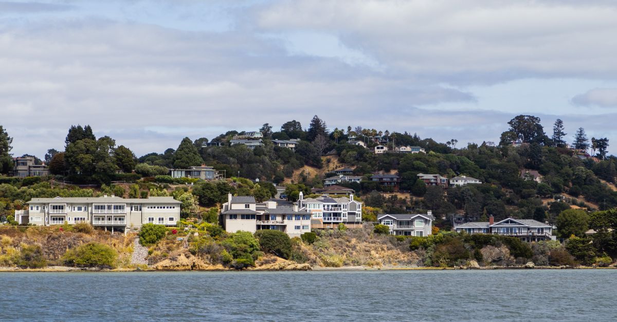 Picturesque view of coastal hillside houses surrounded by lush greenery and waterfront.