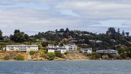 Free Picturesque view of coastal hillside houses surrounded by lush greenery and waterfront. Stock Photo