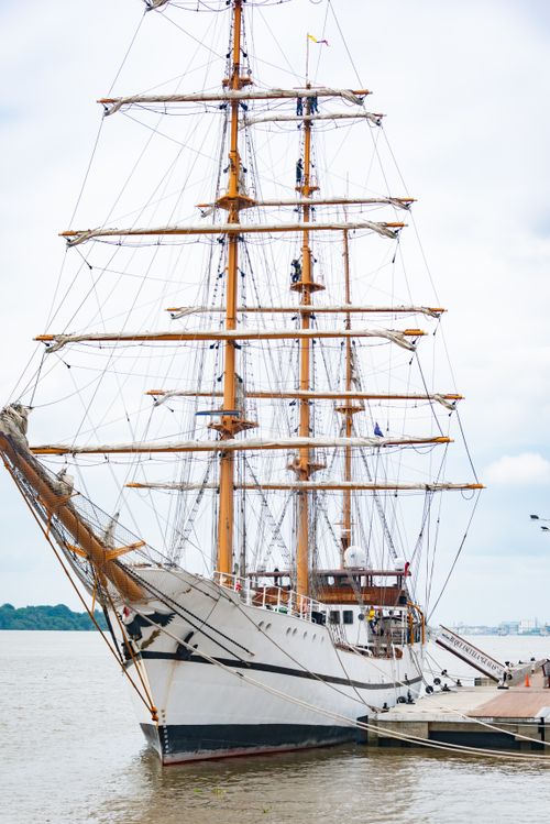 Free A stunning tall ship with sails docked at a bustling harbor on a cloudy day. Stock Photo
