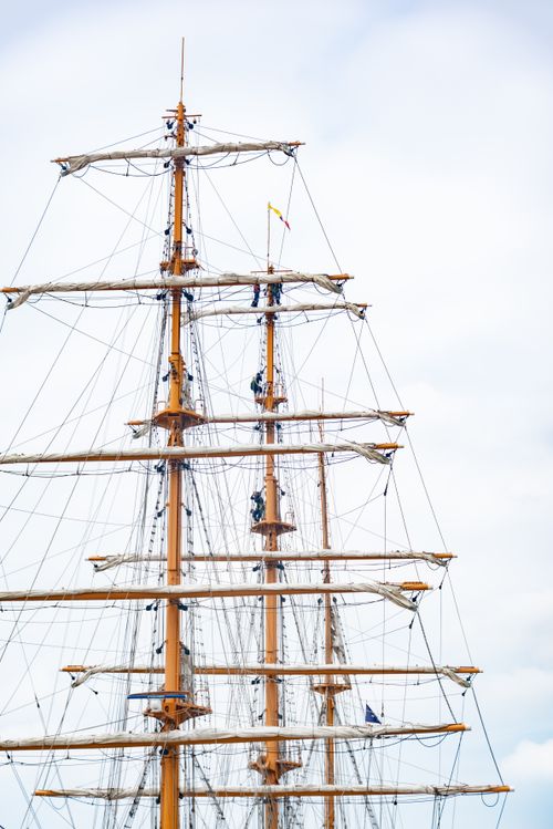 Free Close-up of a tall ship's mast with sailors climbing the ropes against a clear sky. Stock Photo