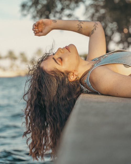 Woman with Tattoos Lying Down on Wall and Posing