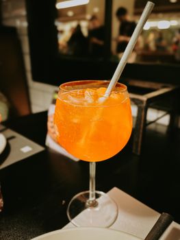 Vibrant orange cocktail with ice and straw in a stylish wineglass.