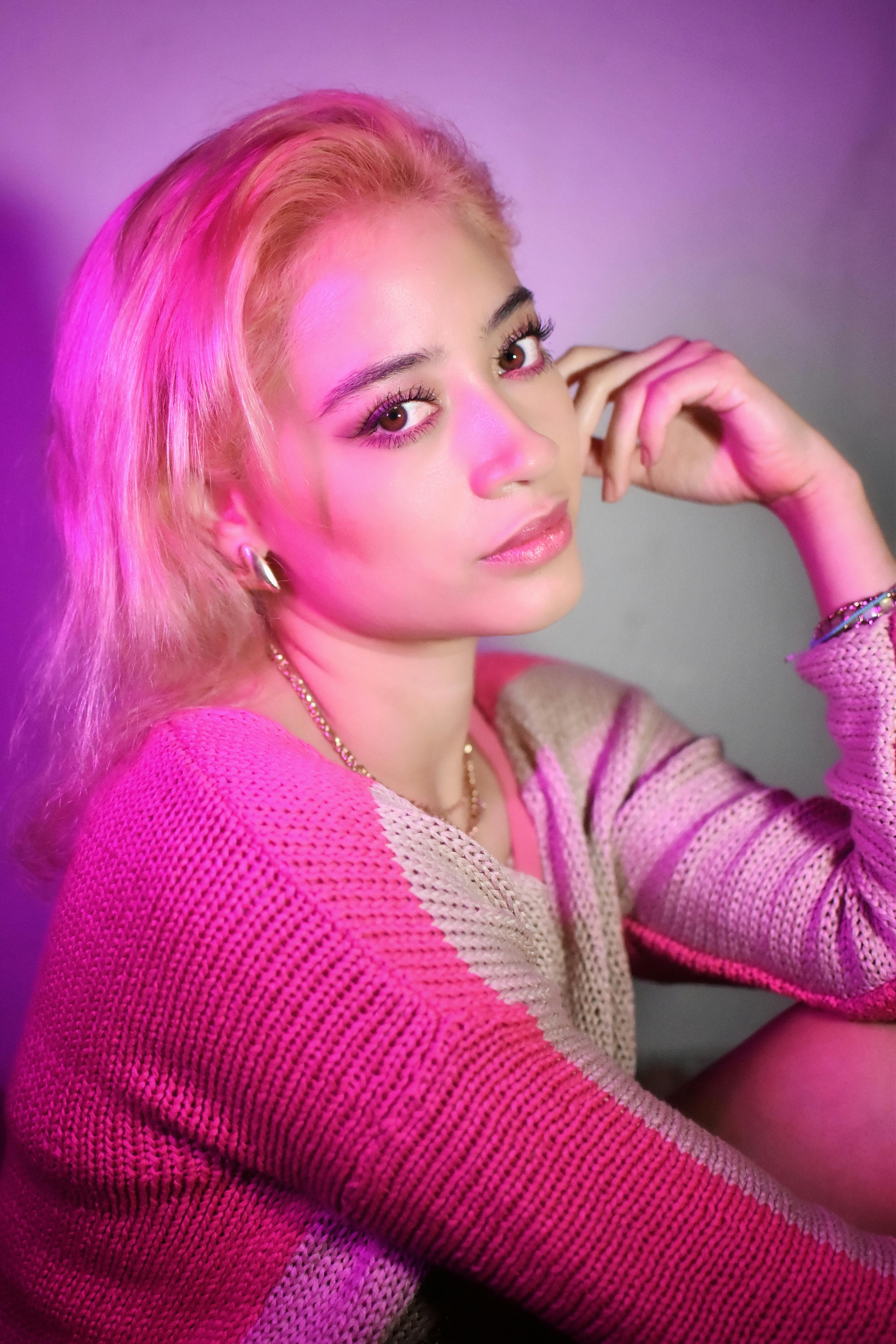 Artistic portrait of a blonde woman in vibrant pink lighting, wearing a knitted sweater.