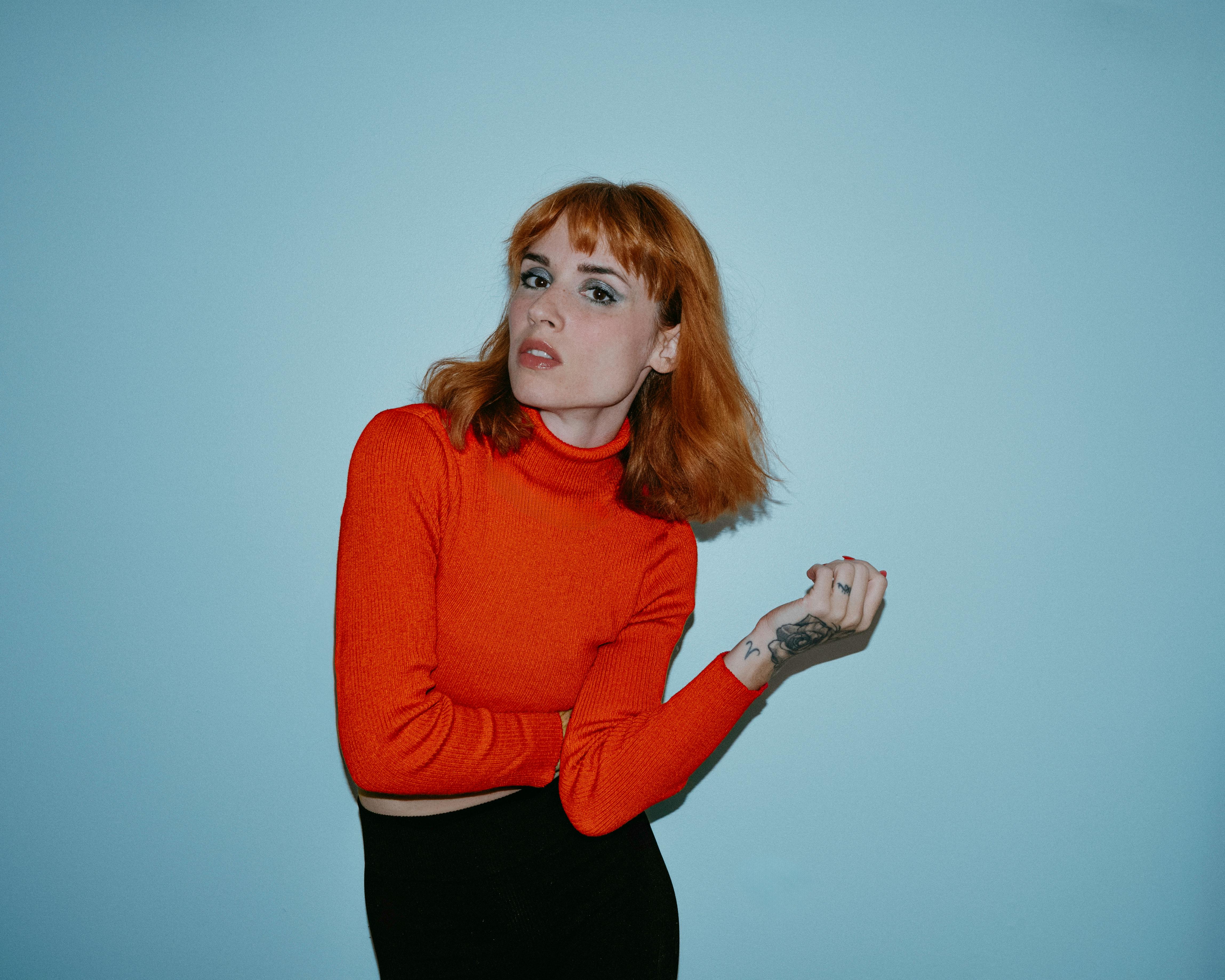 Portrait of a stylish adult woman in a red turtleneck sweater against a blue background.