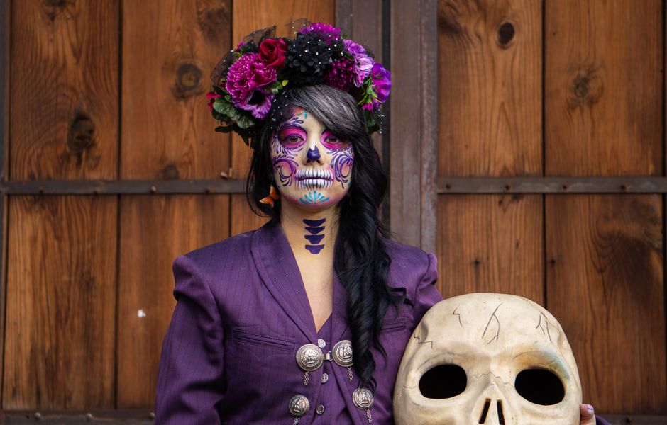 A woman in skull makeup poses with traditional Mexican attire celebrating Day of the Dead.