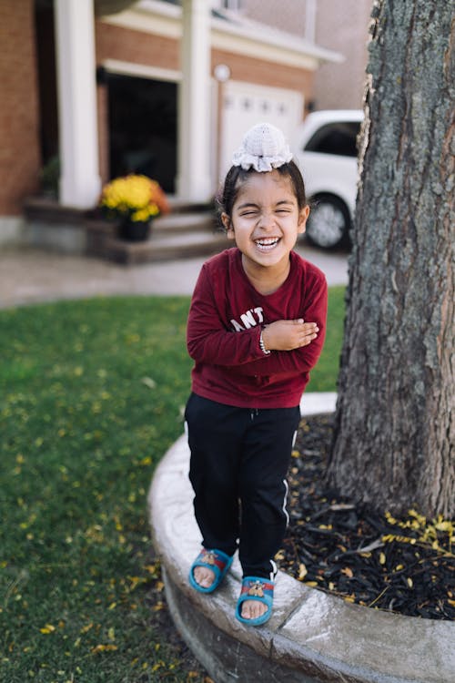 Free A little girl smiling while standing next to a tree Stock Photo