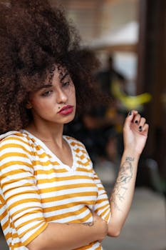 Portrait of a fashionable woman with curly hair and tattoos wearing a striped top, striking a pose.