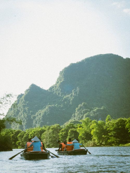 Free Tourists enjoy a calm river ride with stunning views of lush green mountains in Vietnam. Stock Photo