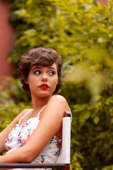 Stylish woman with red lipstick and short hair in a floral dress sitting outdoors.