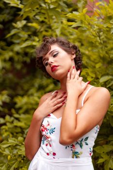 Graceful woman with red lipstick and floral dress posing amidst lush greenery.