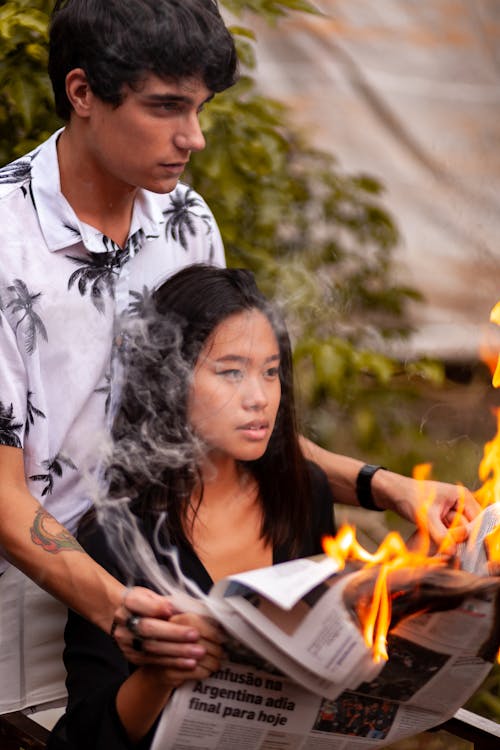 Pria Berdiri Di Belakang Wanita Sambil Memegang Tangannya Dengan Koran Terbakar