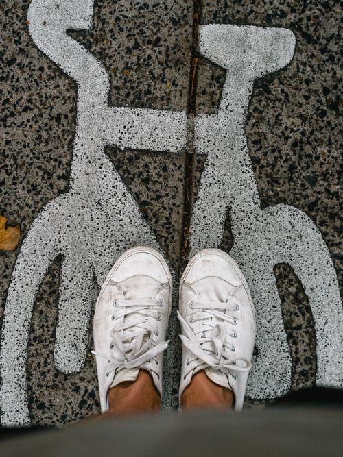 Free Close-up of white sneakers on a bike lane sign. Perfect for urban themes. Stock Photo