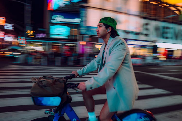 Man In Jacket And Cap Riding Bike On Street At Night