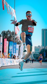 Energetic runner leaps midair during marathon event in an urban setting.