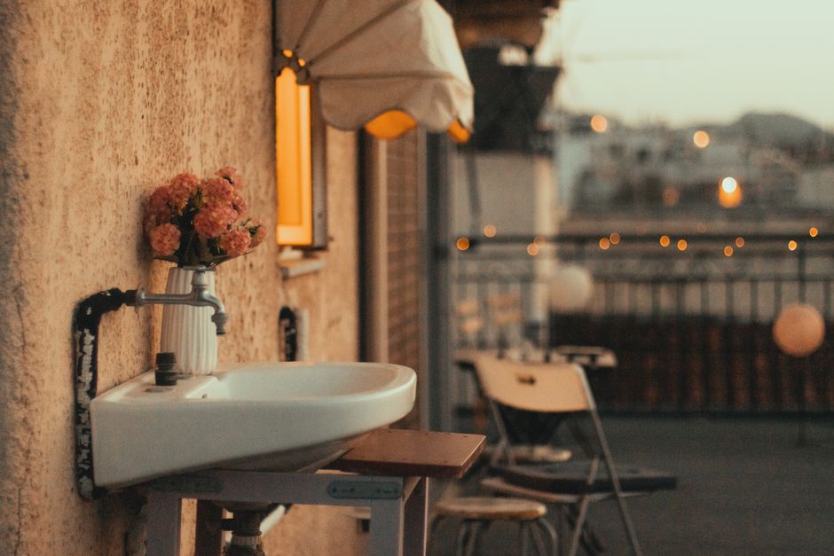 Photo by Chrys Stam on Pexels Cozy outdoor setting with sink, flowers, chairs, and evening city lights.
