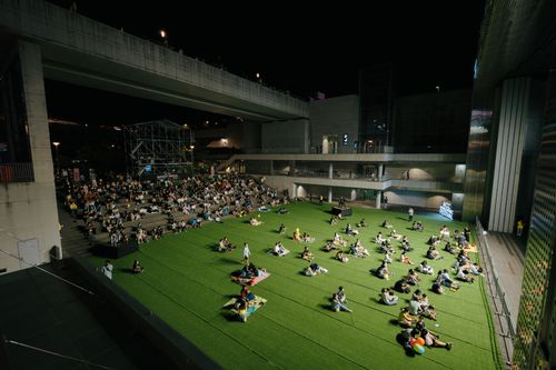 Free A vibrant night event with people gathered on artificial grass under a modern structure. Stock Photo