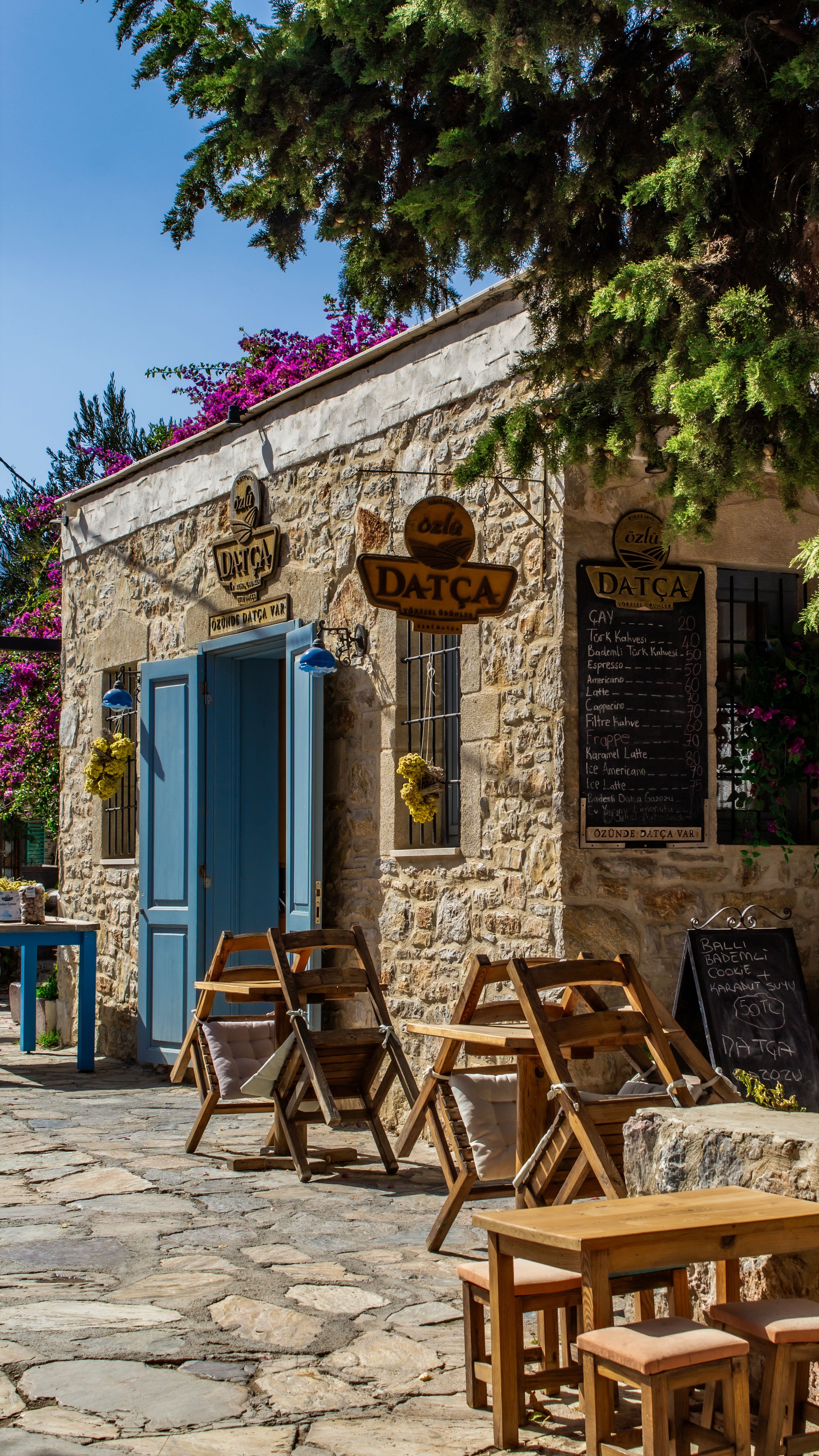 Rustic outdoor café with wooden furniture and stone walls in sunny Datça, Türkiye.
